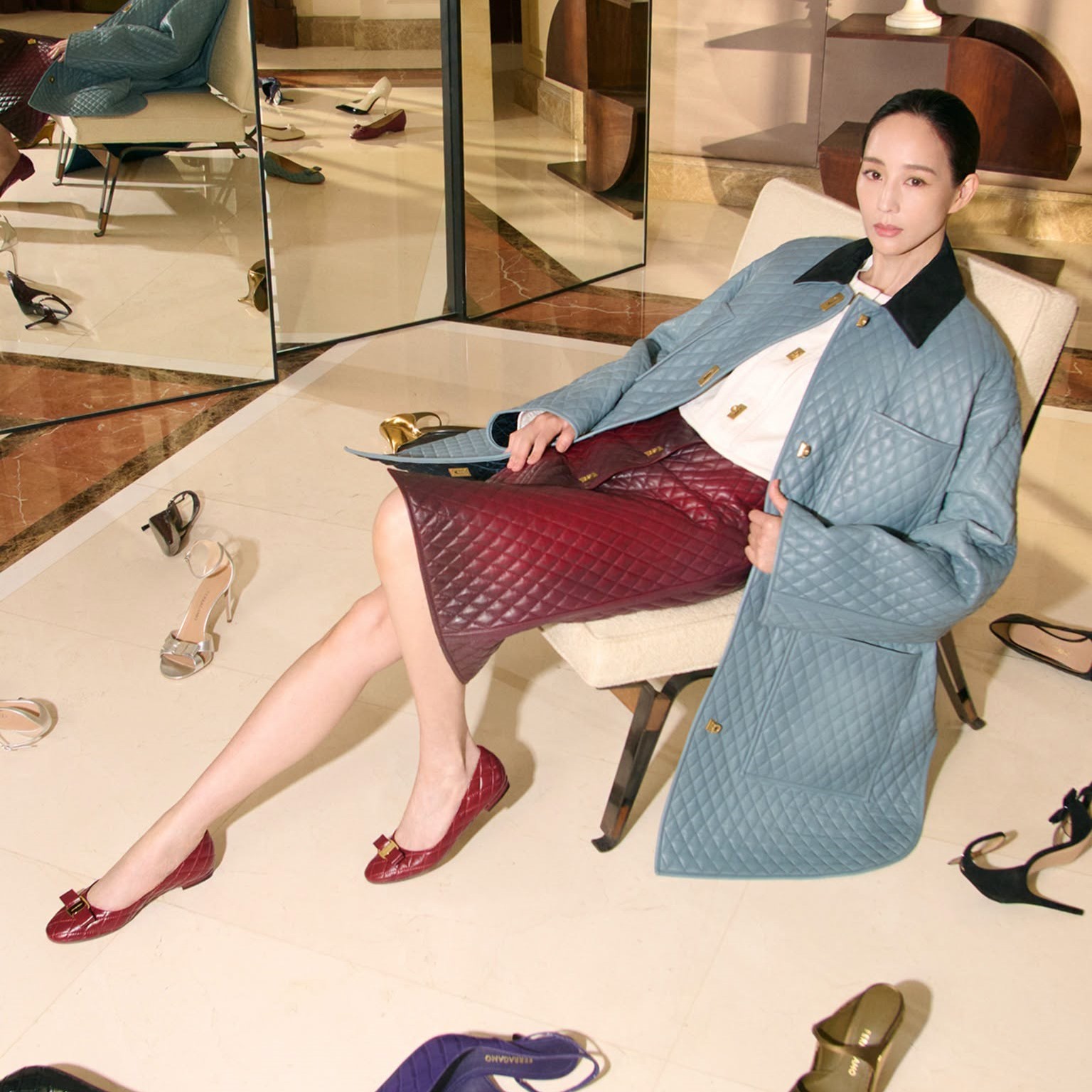 Ning Chang seated on the floor wearing a grey coat, carrying Ferragamo's Cara Bag for the Fall-Winter 2026 campaign