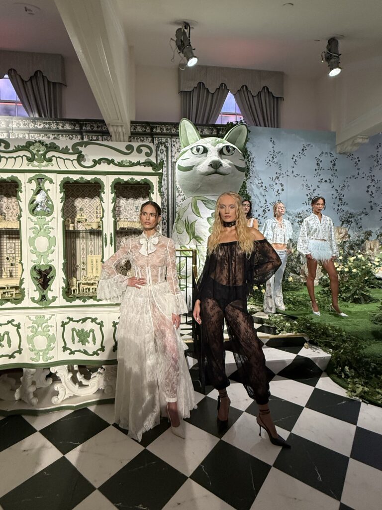 Models wearing white and black lace looks inside the Alice + Olivia Spring/Summer 2027 Wonderland presentation.