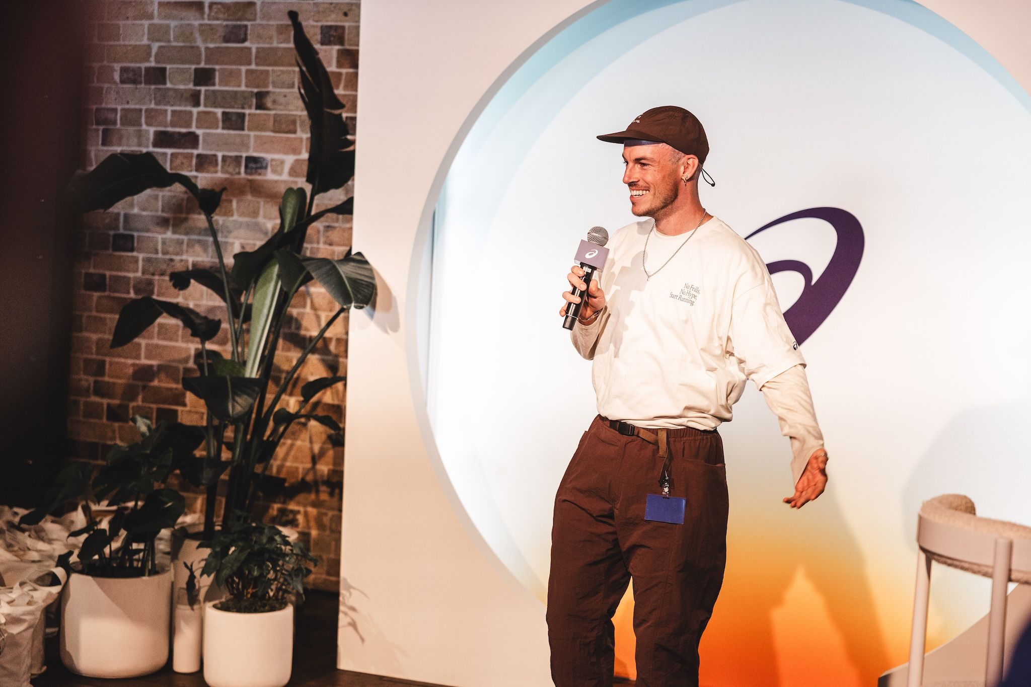 Speaker holding a microphone in front of the ASICS display