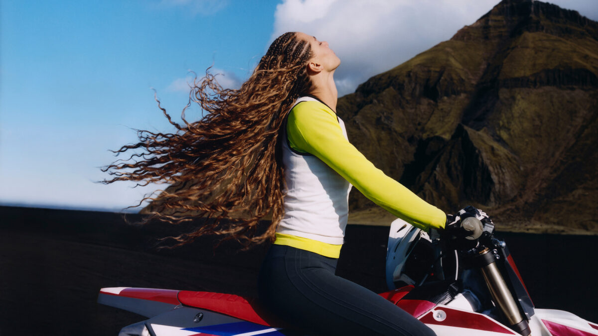 Athleta campaign athlete seated on a motorcycle in a mountain landscape.