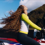Athleta campaign athlete seated on a motorcycle in a mountain landscape.