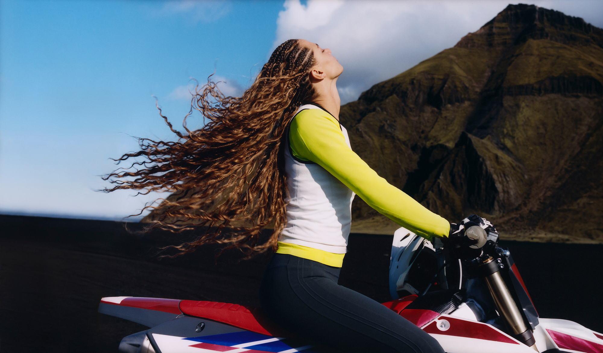 Athleta campaign athlete seated on a motorcycle in a mountain landscape.