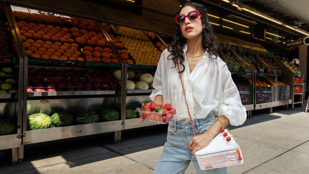 Model carrying the pink Betty Ate Strawberry Cake handbag outside a produce store