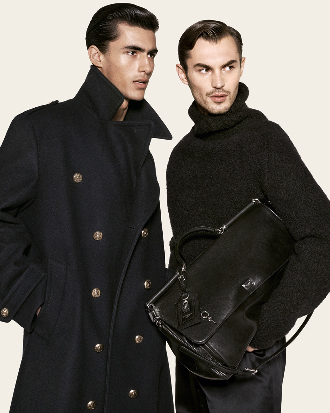 Two models in dark outerwear and knitwear with a leather bag