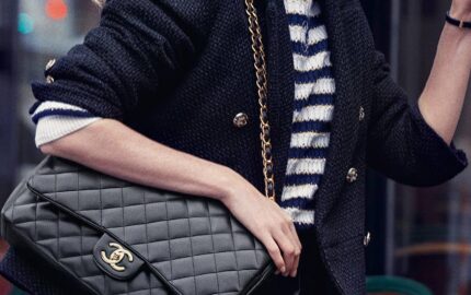 Model wearing a black CHANEL jacket and carrying a quilted CHANEL handbag in campaign imagery.