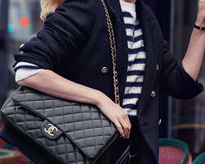 Model wearing a black CHANEL jacket and carrying a quilted CHANEL handbag in campaign imagery.