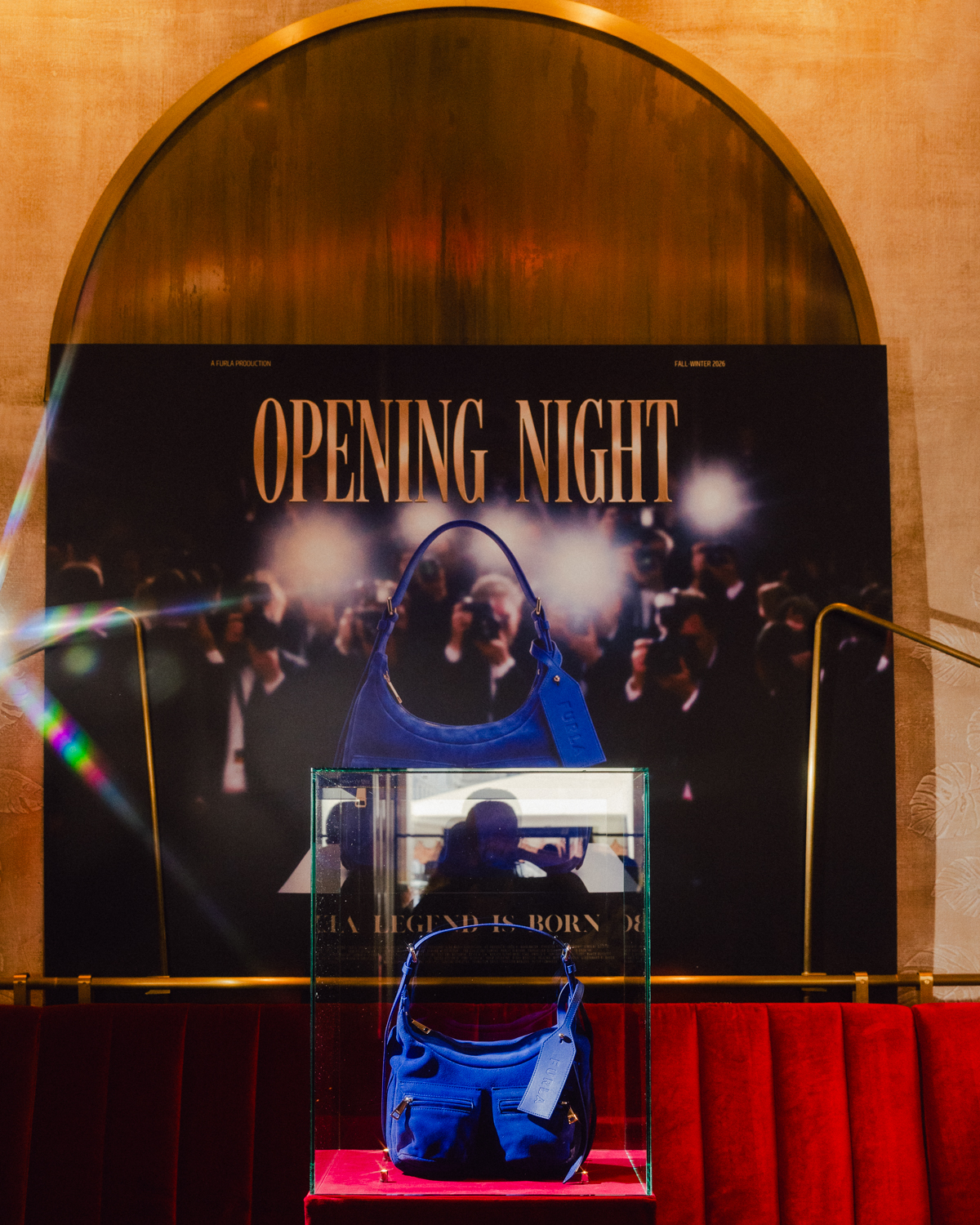 Blue Furla Lynette bag displayed against an Opening Night movie poster