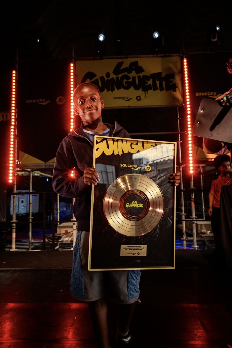 Attendee holds a JD Sports and Saucony Guinguette gold-record prize