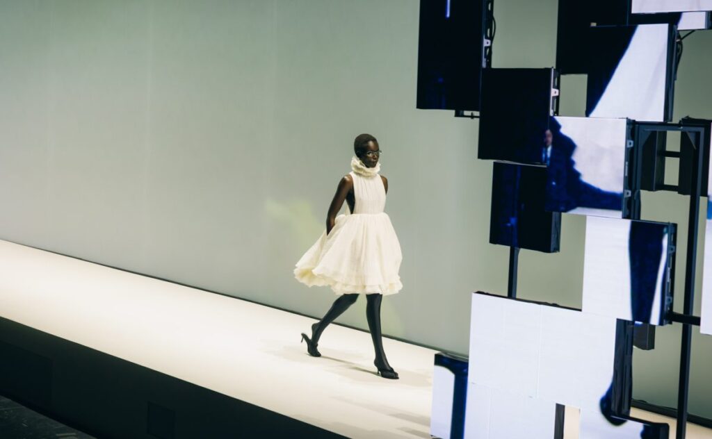 Model in a white look on the H&M London Fashion Week 2026 runway beside a screen installation
