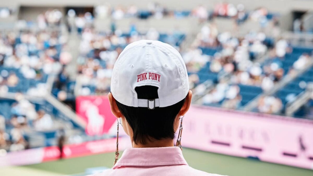 Guest wearing a white Pink Pony cap overlooking the US Open court.