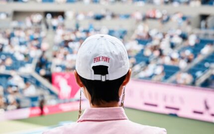 Guest wearing a white Pink Pony cap overlooking the US Open court.
