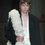Model wearing black tailoring with a white floral accessory at Simone Rocha’s Spring Summer 2027 menswear show.
