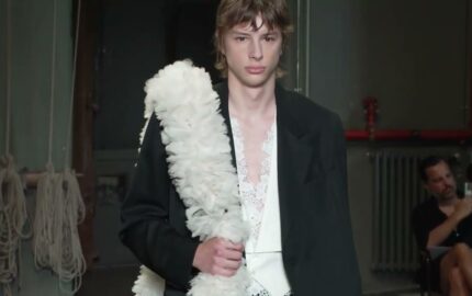 Model wearing black tailoring with a white floral accessory at Simone Rocha’s Spring Summer 2027 menswear show.