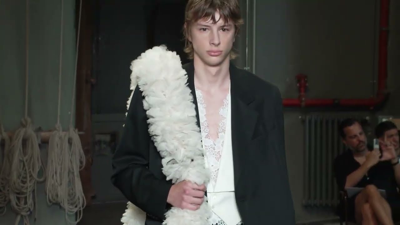 Model wearing black tailoring with a white floral accessory at Simone Rocha’s Spring Summer 2027 menswear show.