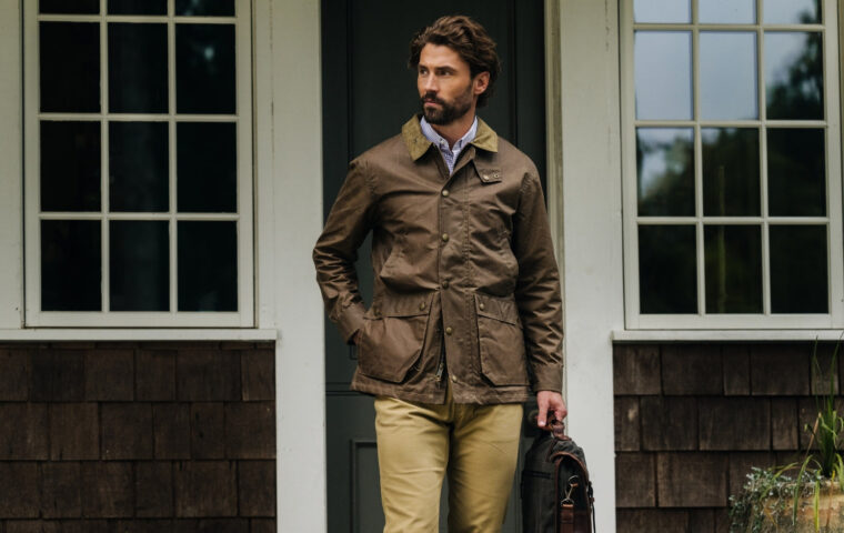 Model wearing a waxed jacket outside a house.