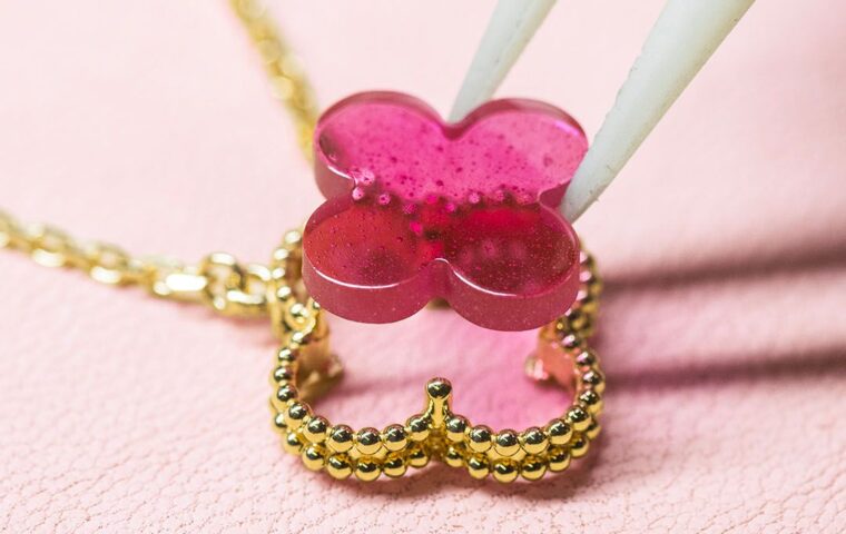 Pink enamel motif being positioned above the gold setting of a Van Cleef & Arpels Alhambra pendant