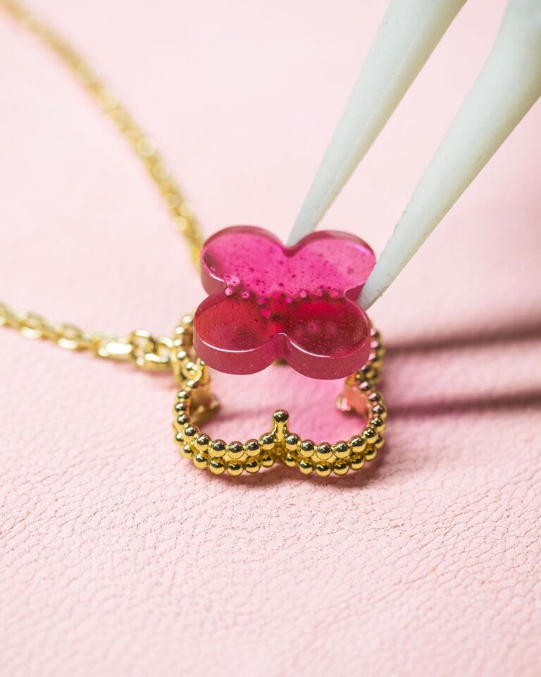 Pink enamel motif being positioned above the gold setting of a Van Cleef & Arpels Alhambra pendant