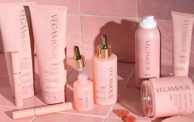 Vegamour haircare products arranged against pink tiles.