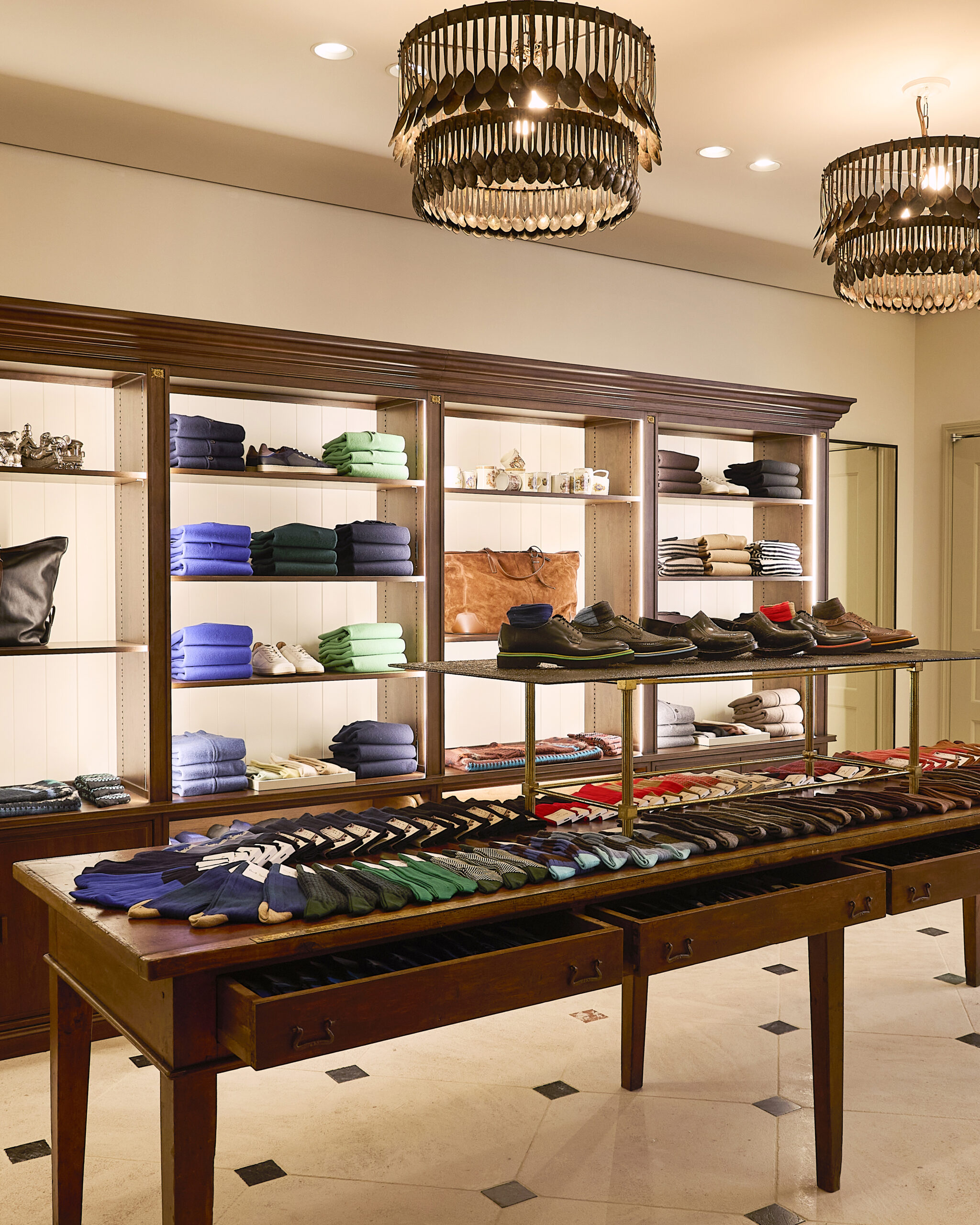 Socks and shoes on a wooden display table beneath spoon chandeliers at Paul Smith Madison Avenue
