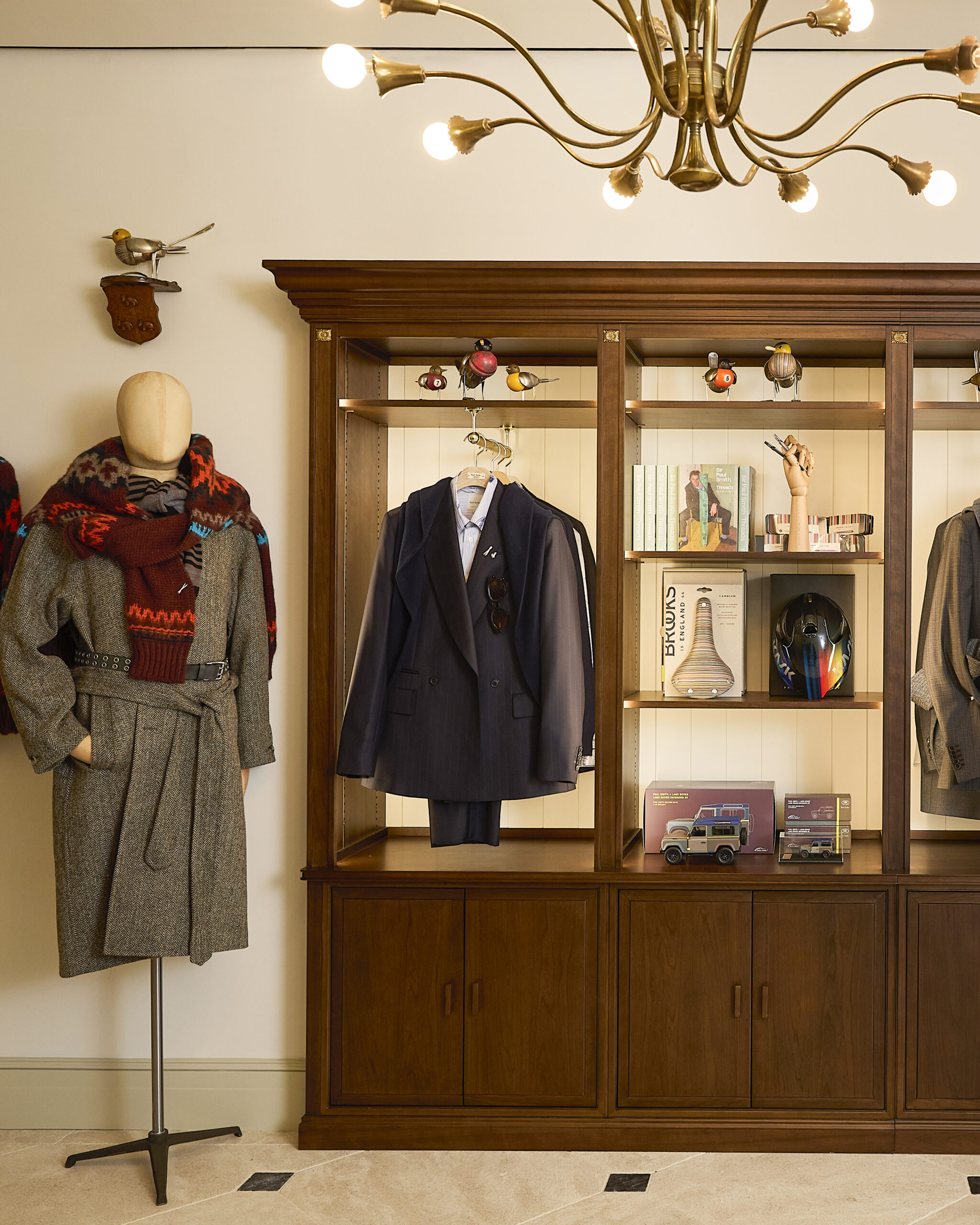 Coats, tailoring and decorative objects displayed in wooden cabinetry at Paul Smith Madison Avenue