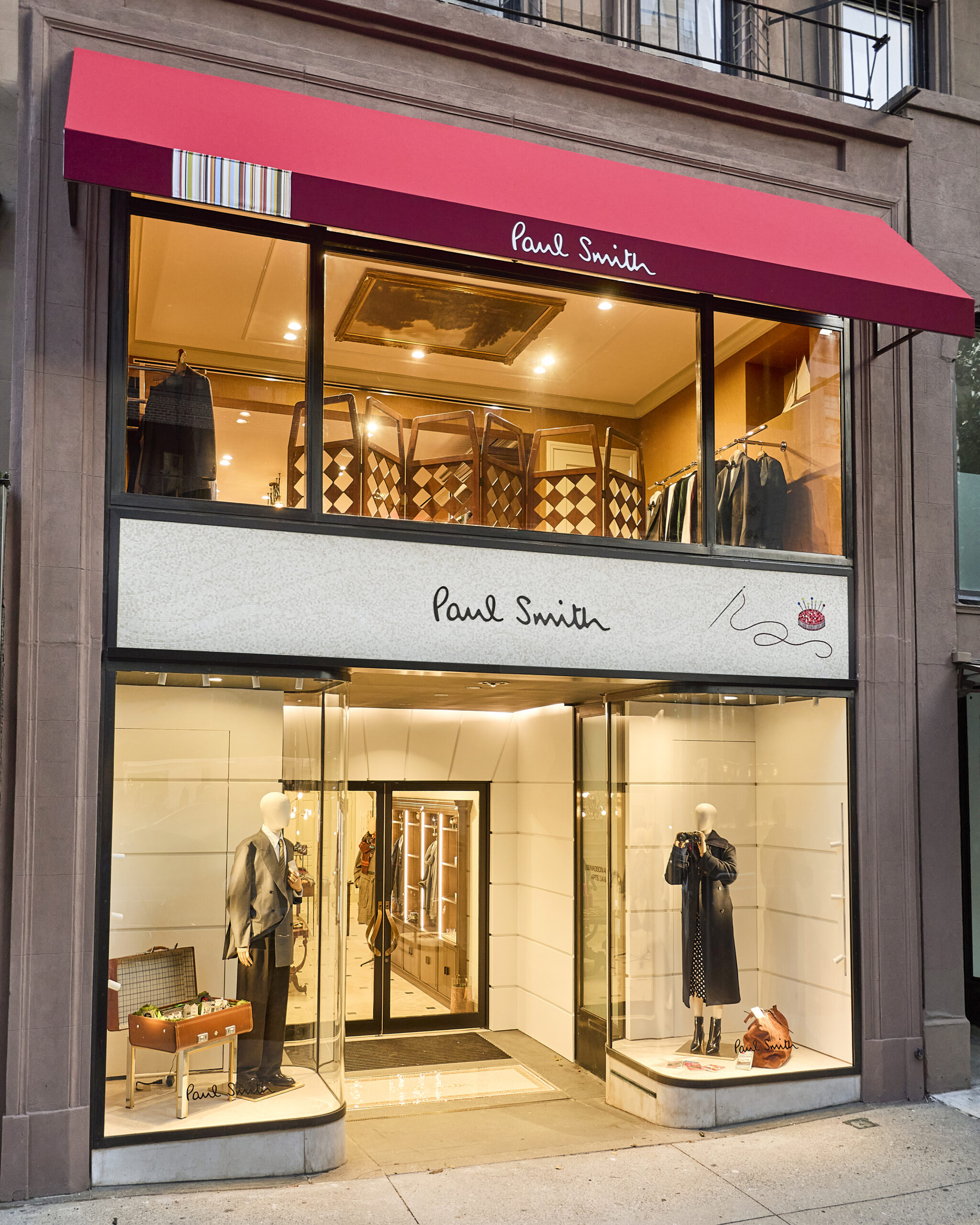 Exterior of Paul Smith’s two-storey Madison Avenue flagship with a red awning and illuminated shop windows