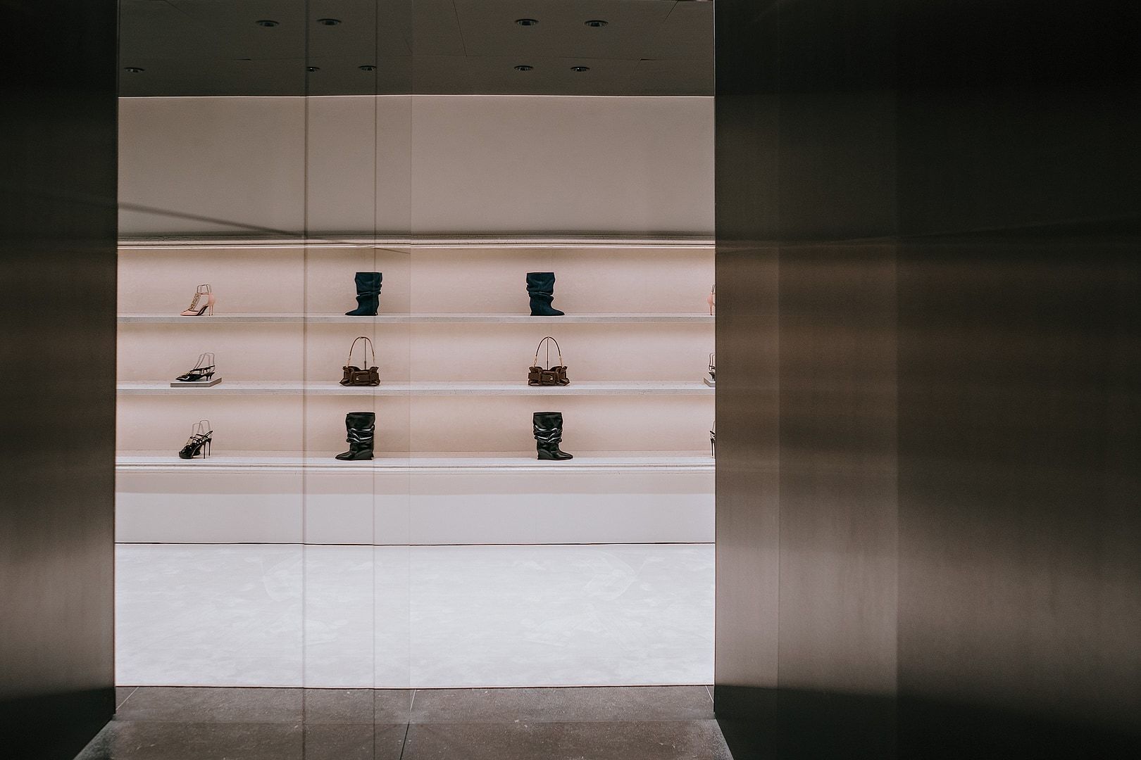Shoes and handbags displayed on illuminated shelves inside Balmain’s Milan flagship