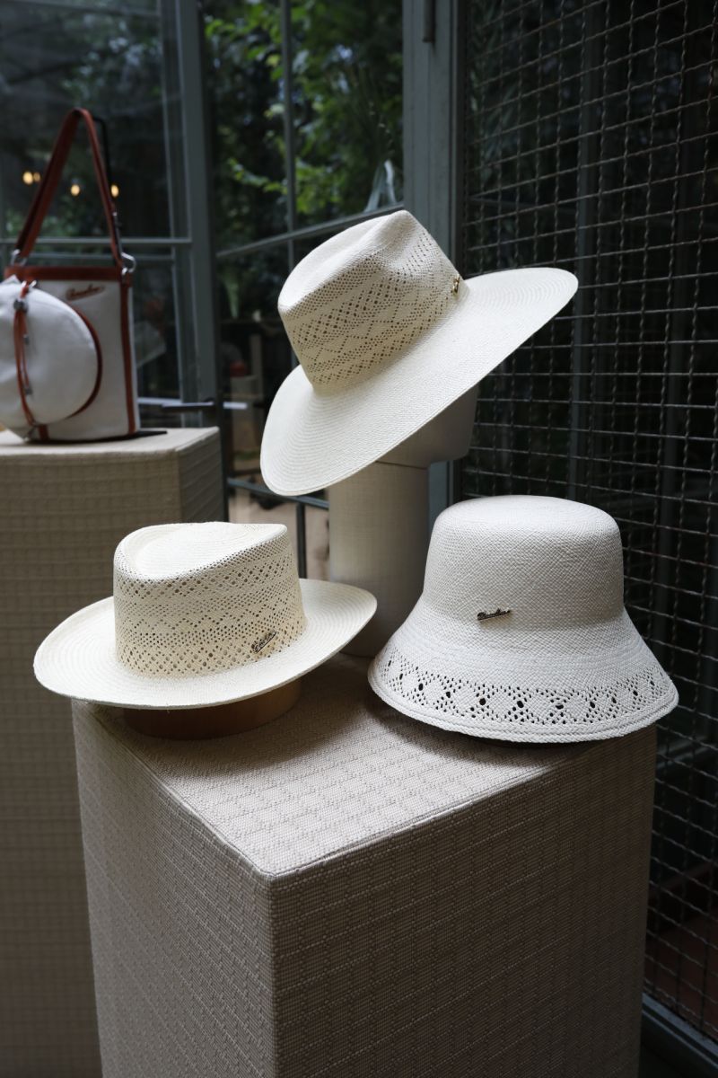 Three white woven Borsalino hats displayed beside a leather bag
