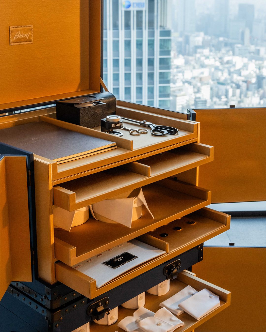 Open Brioni tailoring trunk with tools and shirt samples overlooking Tokyo