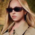 Lila Moss wearing burgundy Burberry sunglasses and a beige trench coat in the Autumn Winter 2026 eyewear campaign