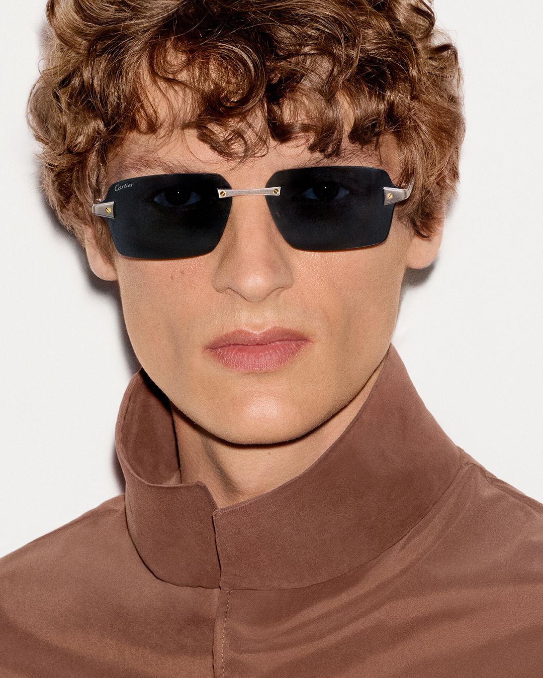 Model wears rectangular dark-lens Cartier sunglasses with metallic screw details