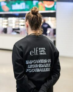 Event representative wearing a jacket branded with e.l.f. and women’s football messaging