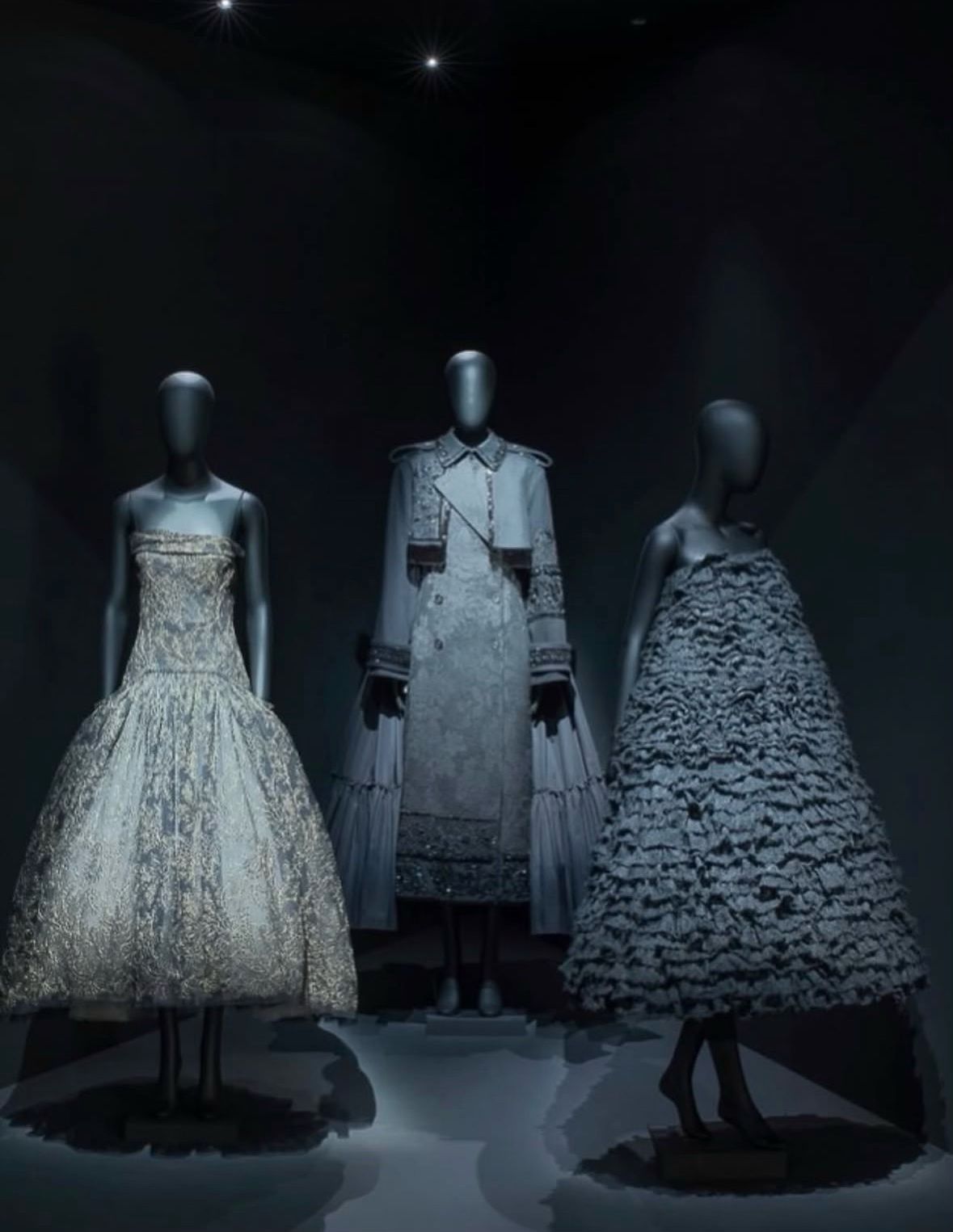 Three ERDEM dresses displayed in a dark exhibition room