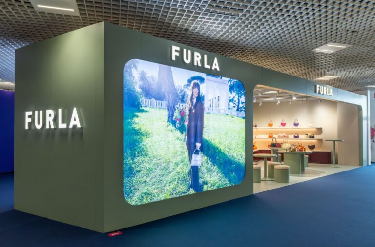Exterior of Furla’s exhibition stand at TFWA 2026 in Cannes, with an illuminated campaign display