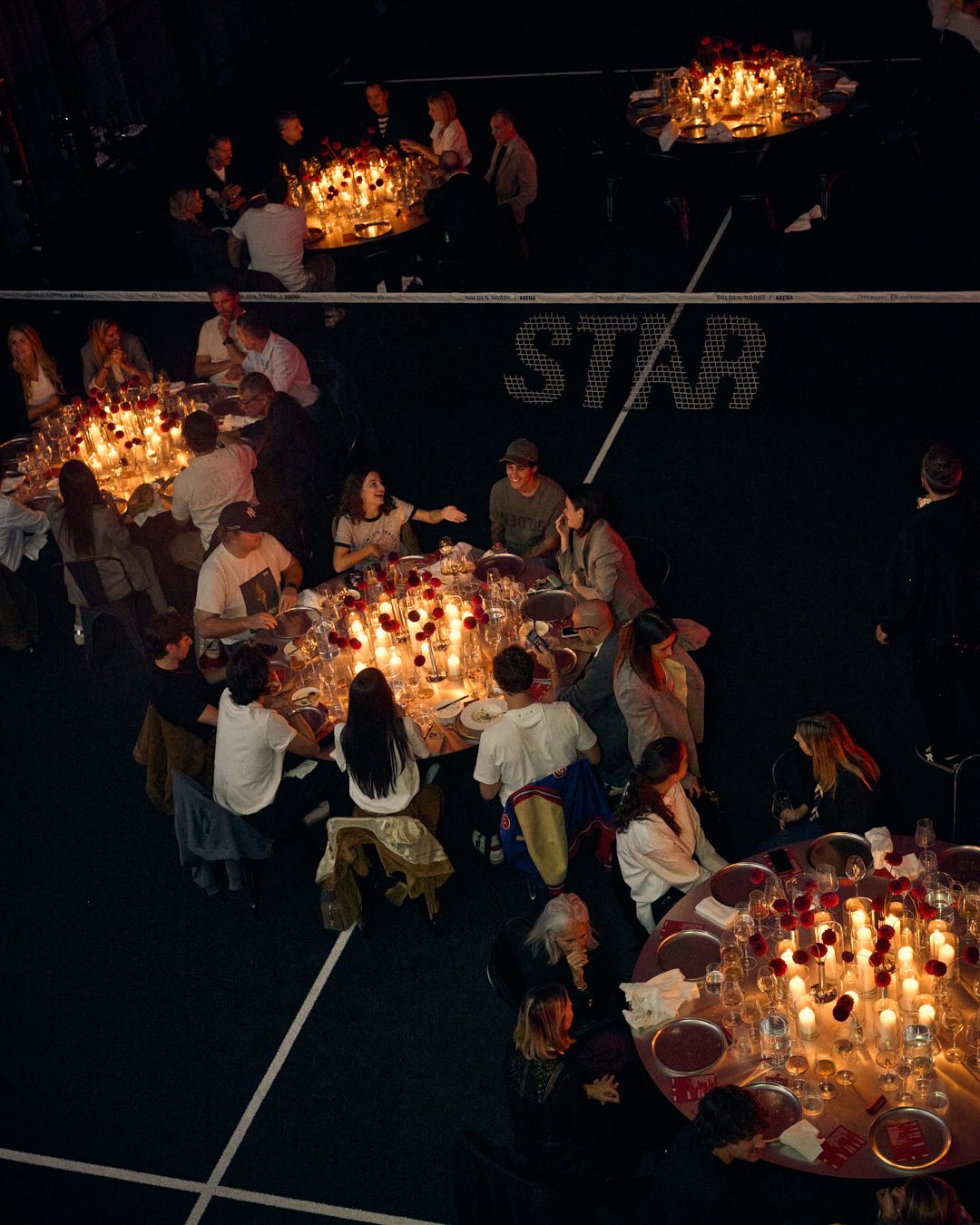 Guests seated around candlelit dining tables on the padel courts at Golden Goose Wild Stars in Milan.
