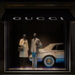 Gucci Primavera mannequins displayed beside a car in a dark flagship window