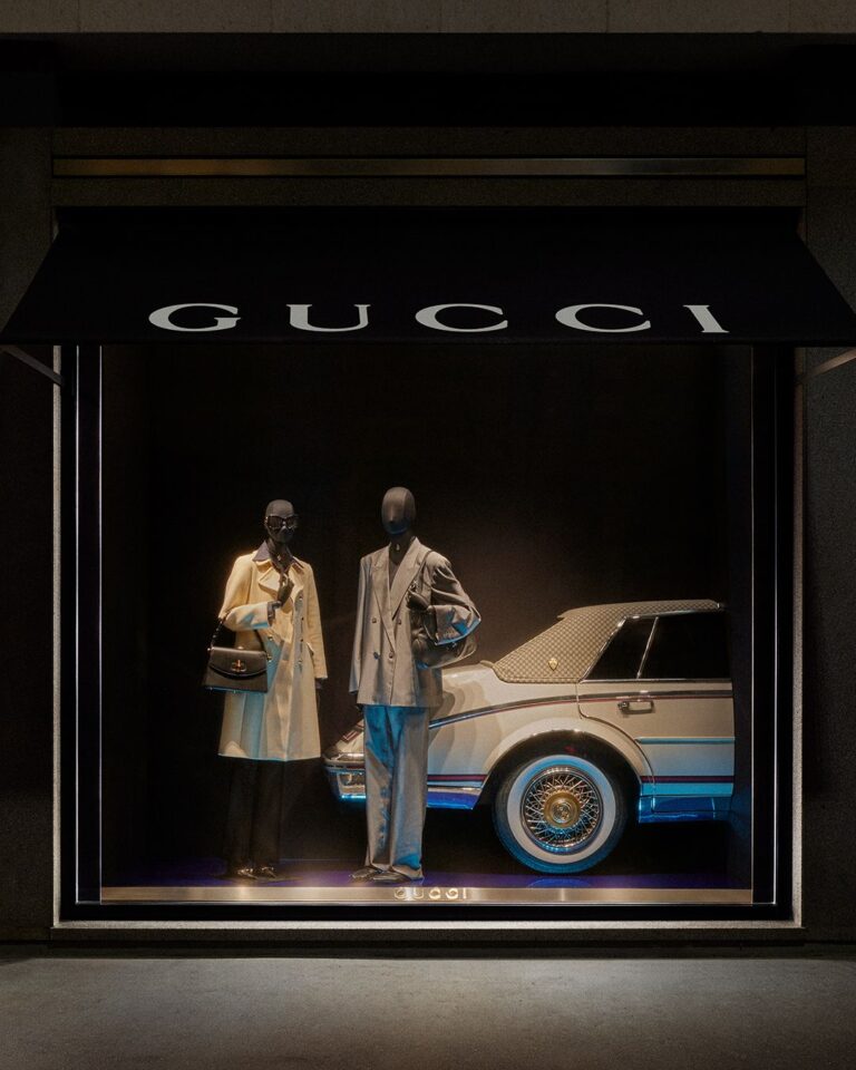 Gucci Primavera mannequins displayed beside a car in a dark flagship window