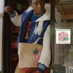 Model wears a KENZO Work and Play varsity jacket and carries a graphic tote