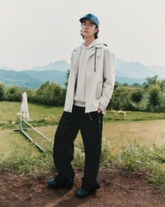 Wang Yibo wearing a cream jacket, dark trousers and blue cap outdoors
