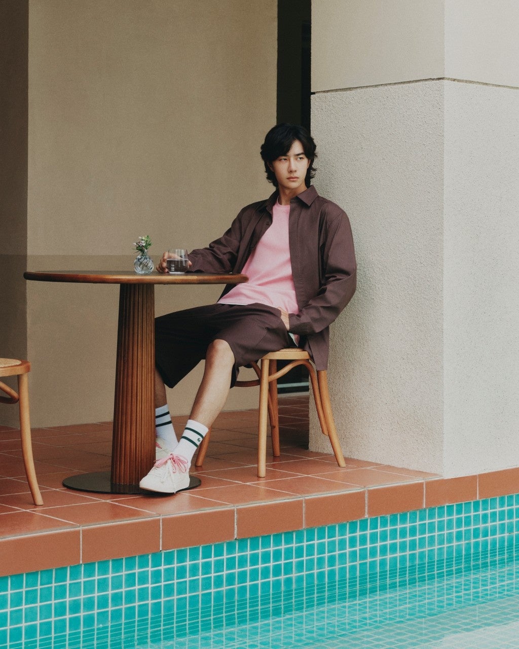 Wang Yibo seated beside a pool in a brown overshirt and shorts with a pink T-shirt