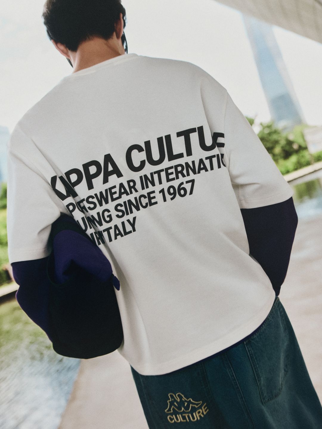 Back of a white Kappa Culture graphic T-shirt and dark denim trousers