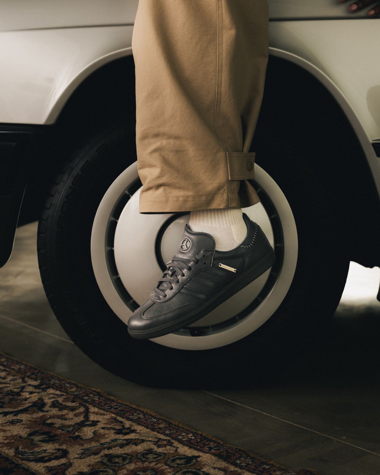 Grey Mercedes-Benz and adidas Samba worn beside a car wheel