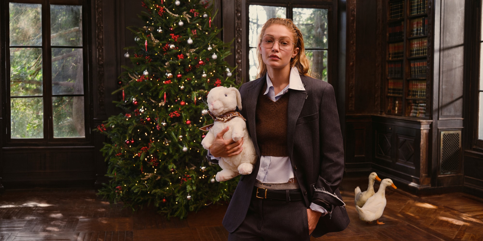 Model holding a plush rabbit beside a Christmas tree for Miu Miu Holiday 2026