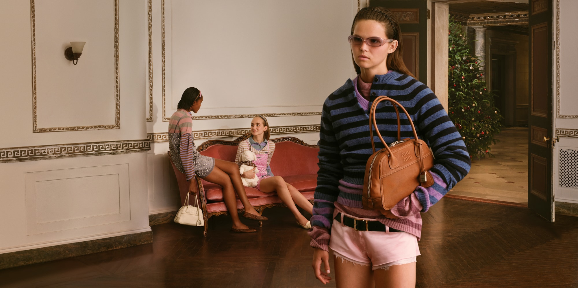 Model in a striped knit carrying a tan handbag in the Miu Miu Holiday 2026 campaign