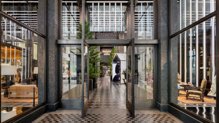 Entrance to Moncler’s Fifth Avenue flagship in New York, with glass doors, dark stone framing and a checkerboard floor.