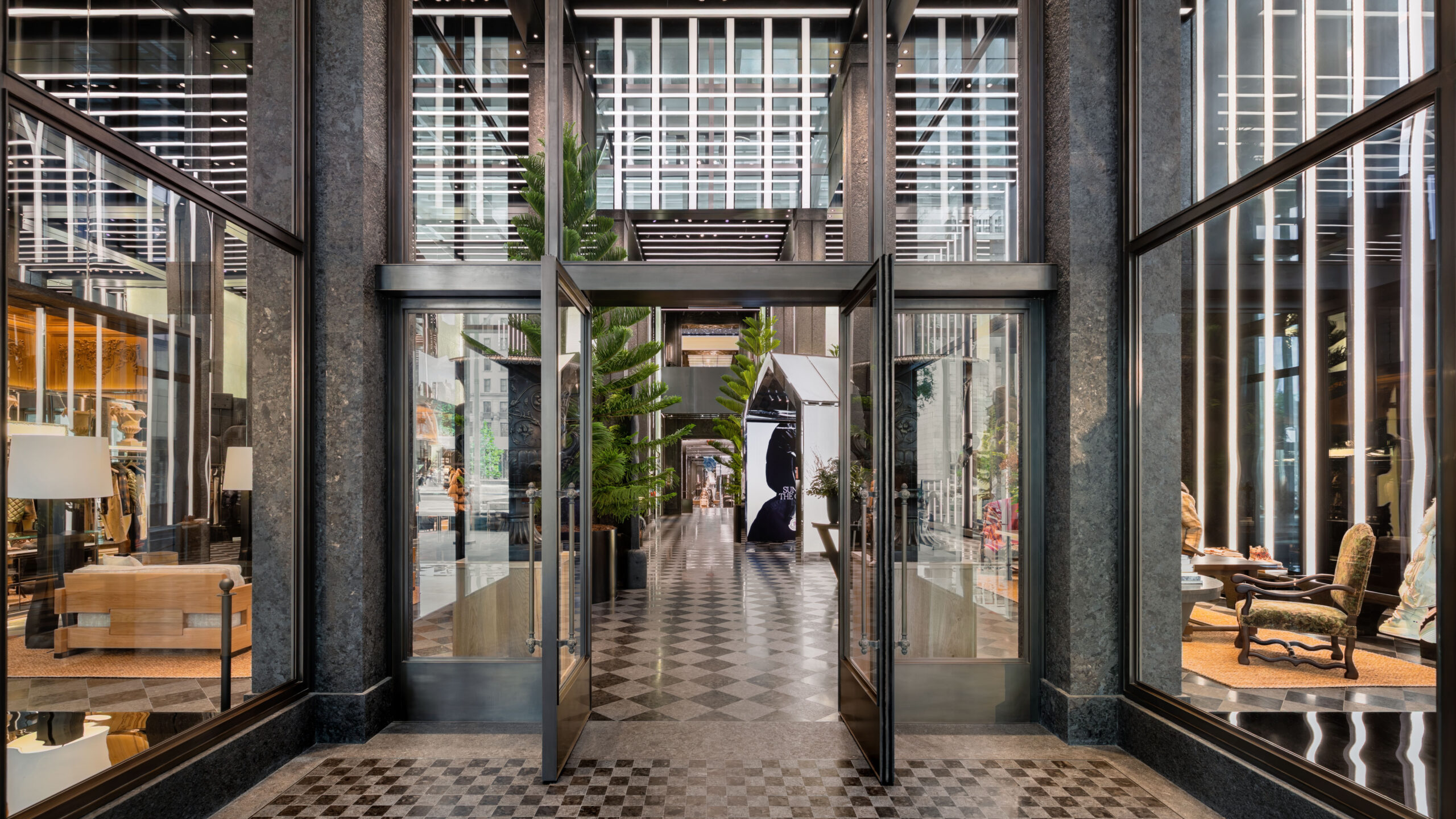 Entrance to Moncler’s Fifth Avenue flagship in New York, with glass doors, dark stone framing and a checkerboard floor.