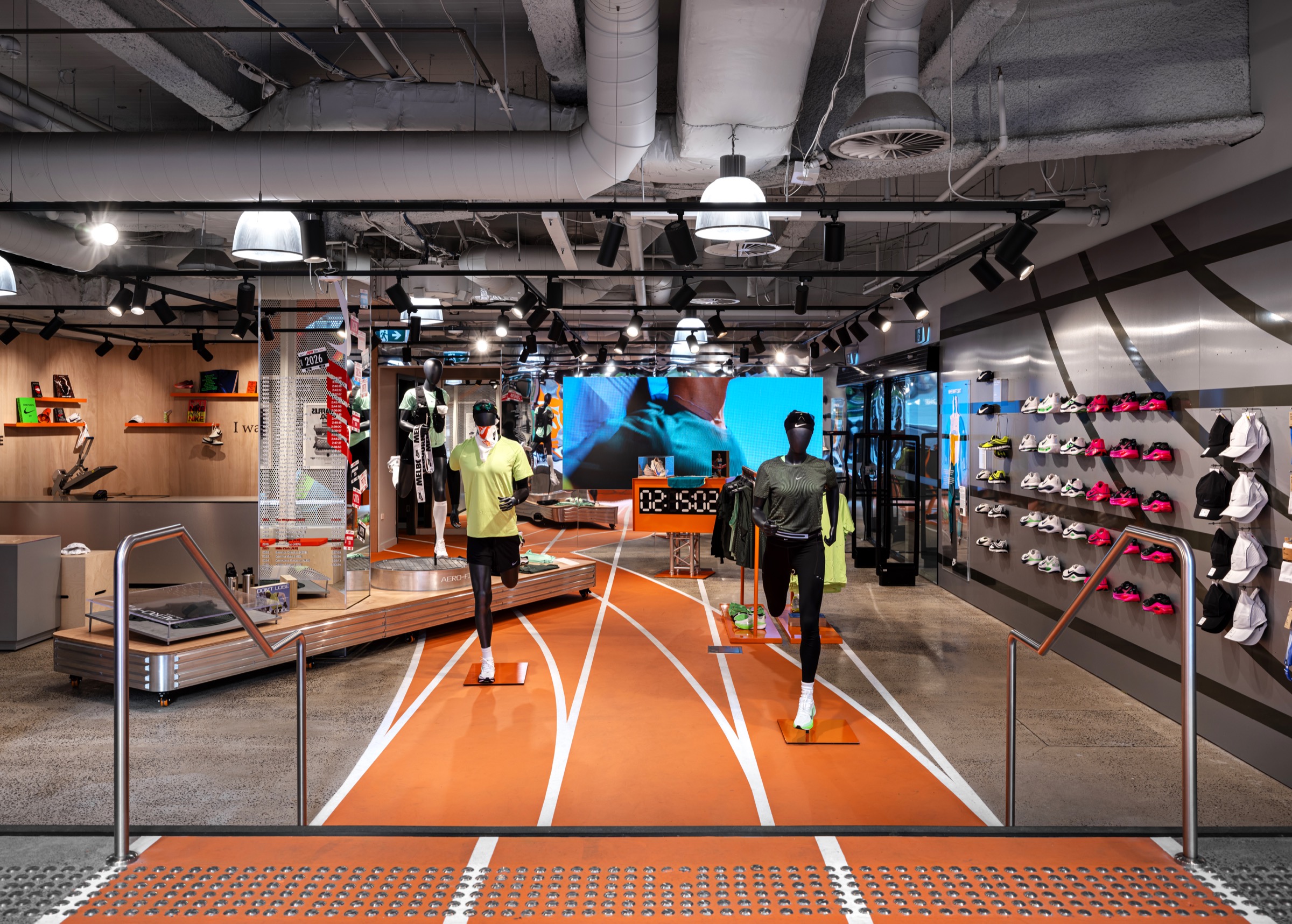 Interior of the Nike Melbourne Central running-led store with an orange track graphic and footwear wall.