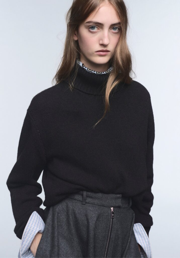 Model in a dark Prada knit sweater with grey trousers