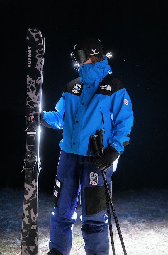 Model in a blue U.S. Ski & Snowboard jacket holding skis