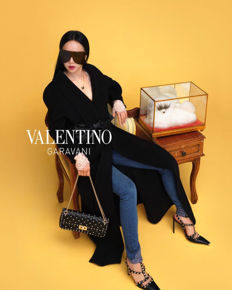 Jolin in black Valentino clothing beside a display case against a yellow backdrop