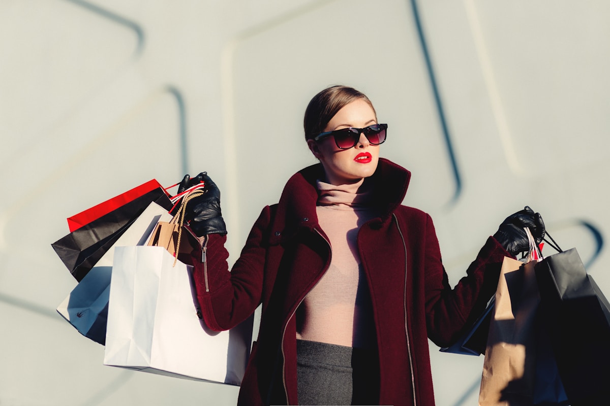Woman in sunglasses and a burgundy coat holding several shopping bags